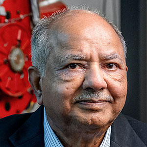 A man in a blue suit sits in front of a red mechanical apparatus