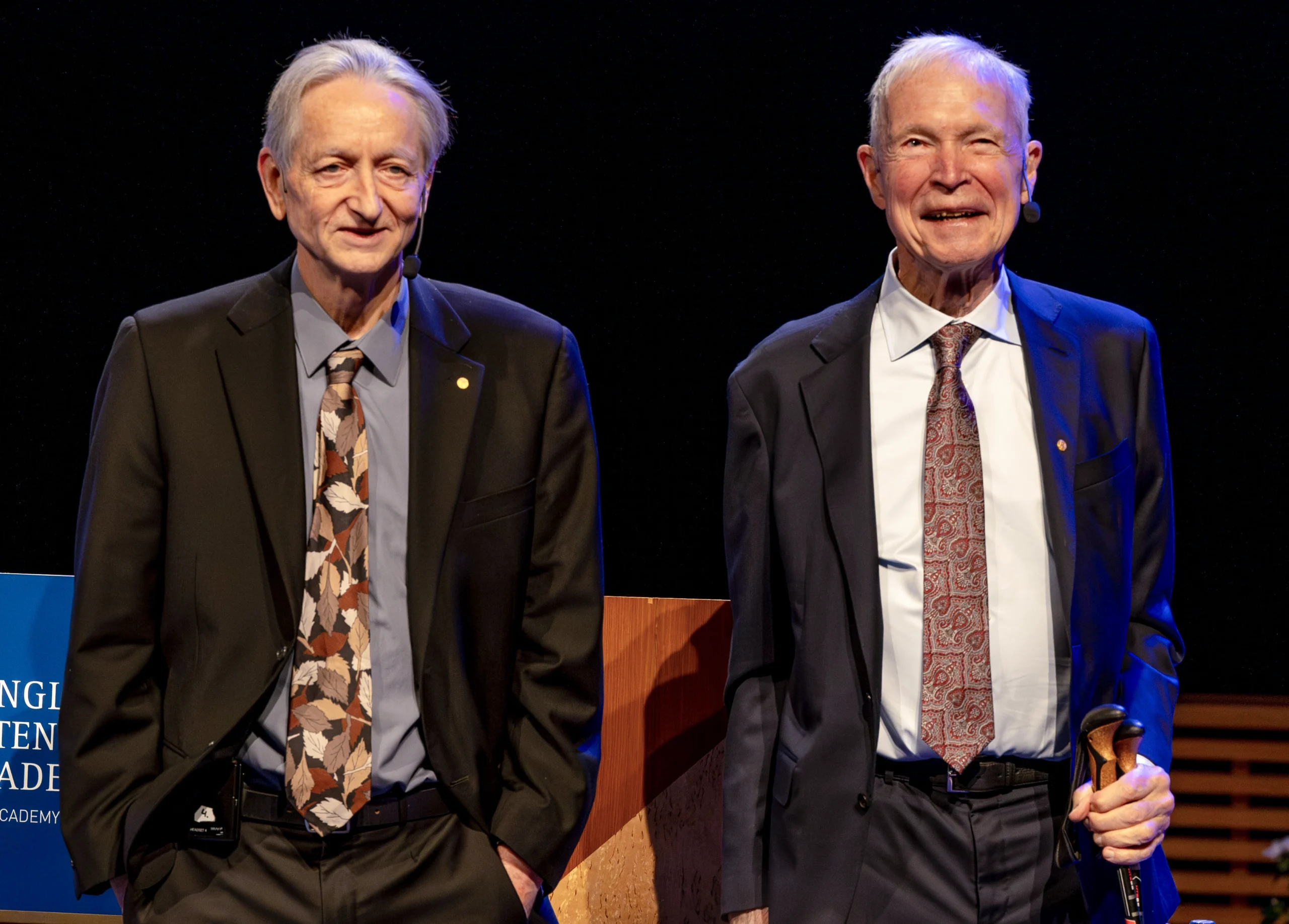 Two smiling men in suits stand side by side.
