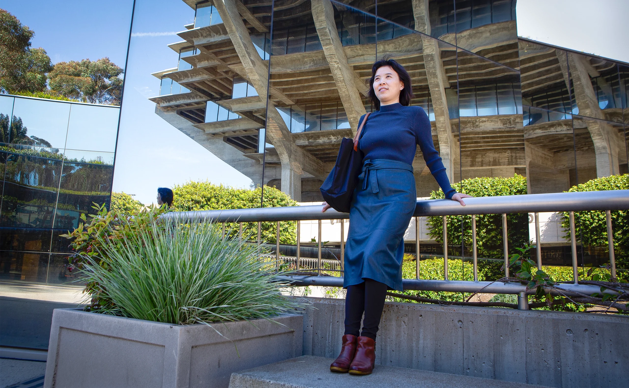 Rose Yu in a dark sweater and skirt leans back on a fence in front of a series of mirrors.