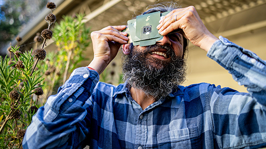 Manu Prakash holds a paper microscope to his eye and turns toward the sky.