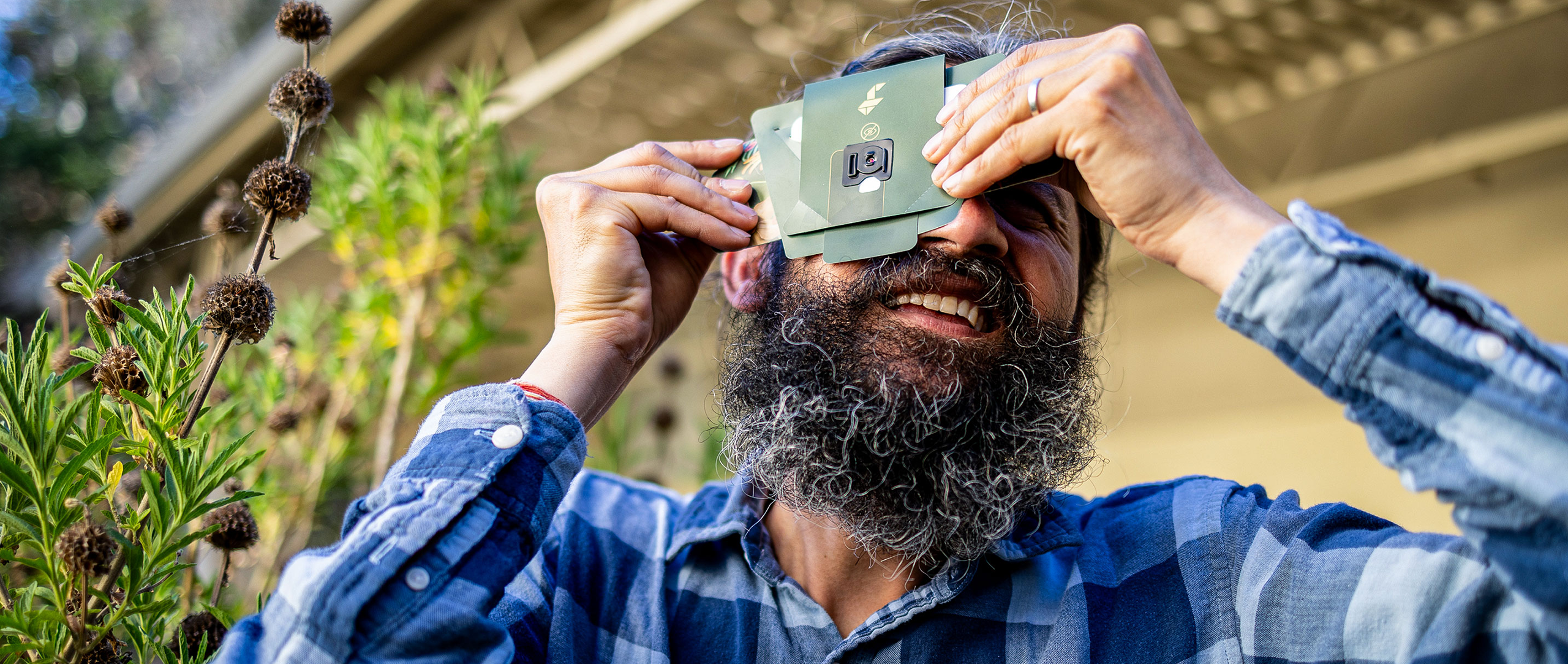 Manu Prakash holds a paper microscope to his eye and turns toward the sky.