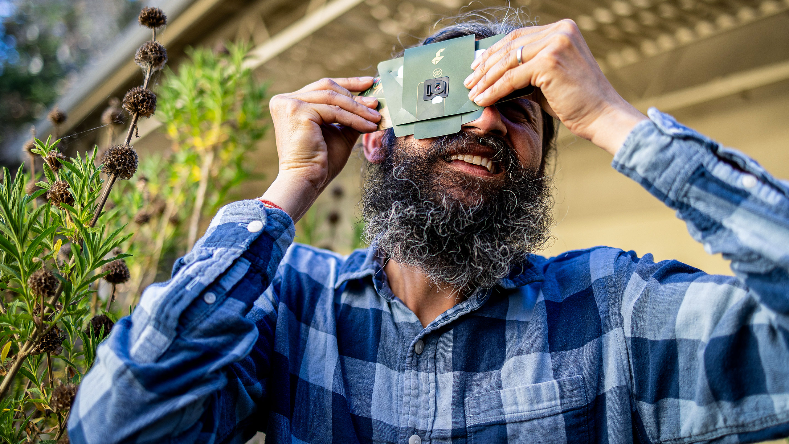 Manu Prakash holds a paper microscope to his eye and turns toward the sky.