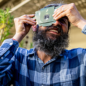 Manu Prakash holds a paper microscope to his eye and turns toward the sky.