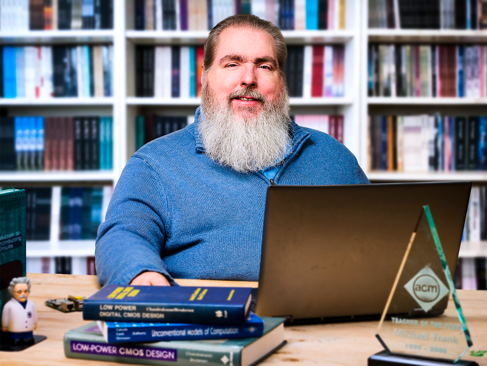 Michael Frank in a blue sweater sits at a desk with a laptop.