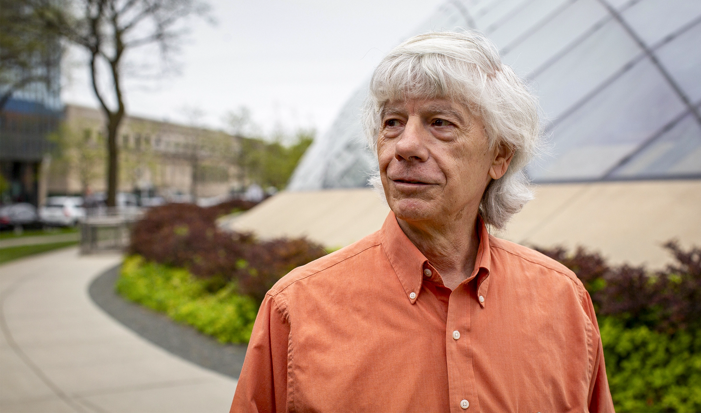 Close-up photo of a man in a bright orange shirt standing outside.