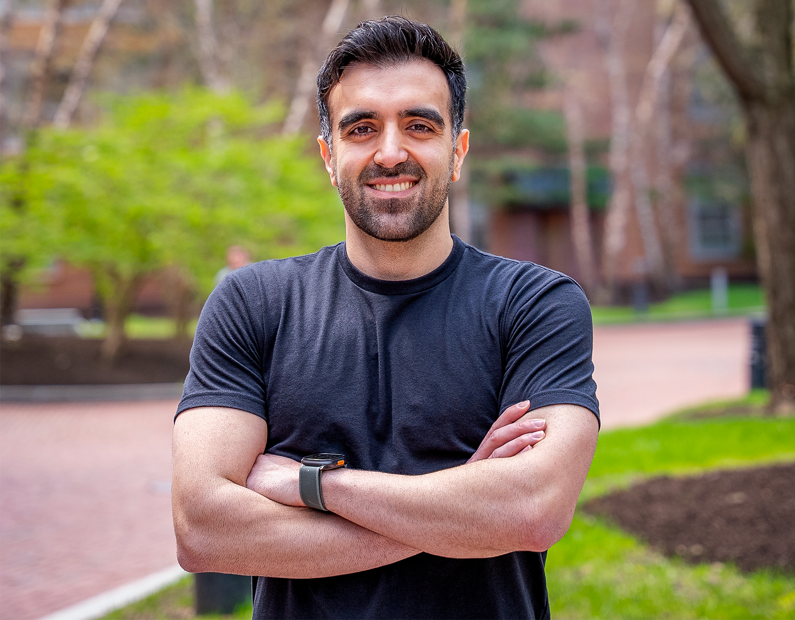 Soheil Behnezhad in a black tshirt stands in front of brown trees