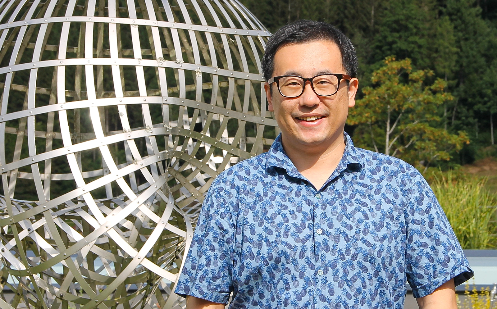 Man in glasses standing in front of sculpture.