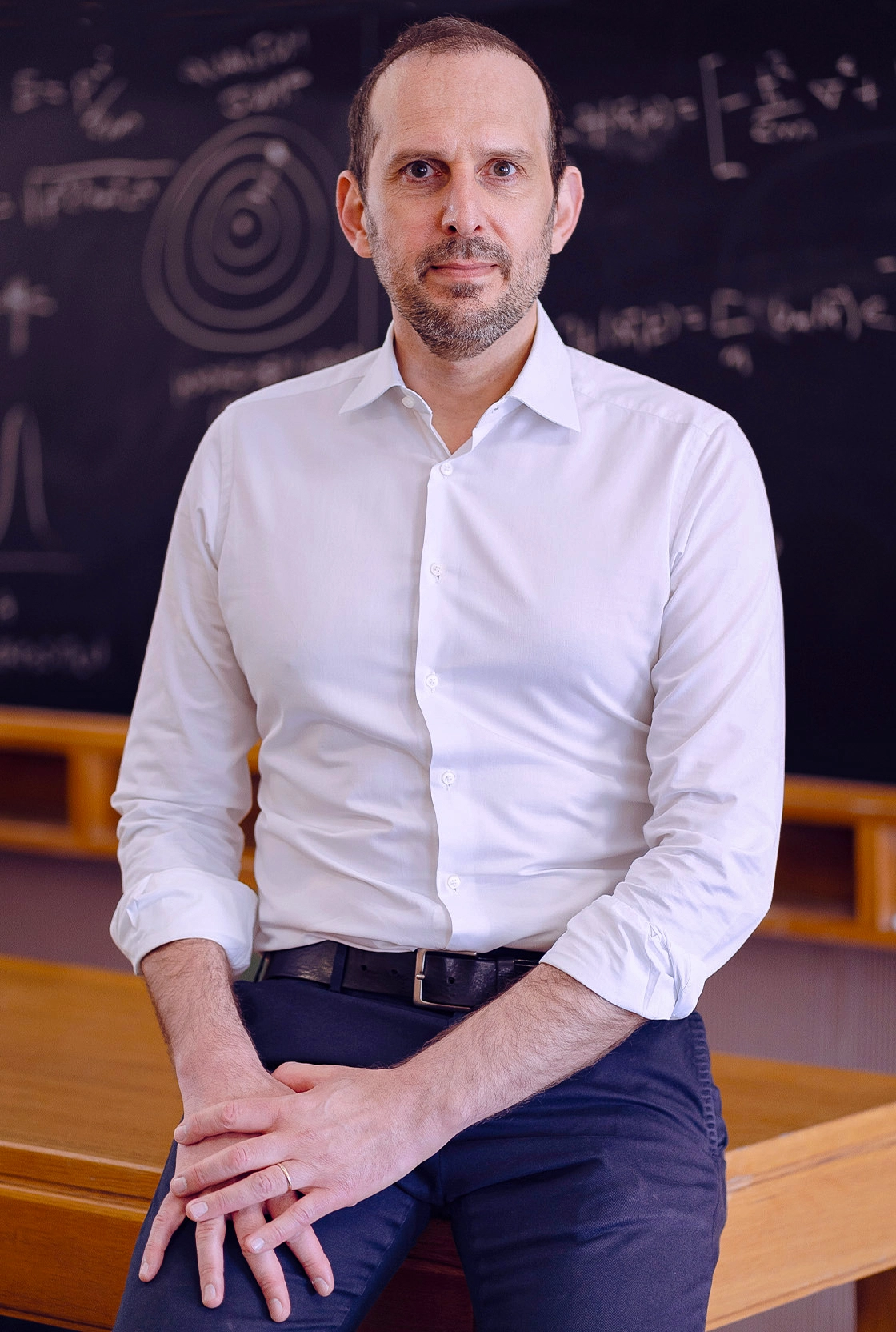 Portrait of a scientist in a white collared shirt sitting on a desk.