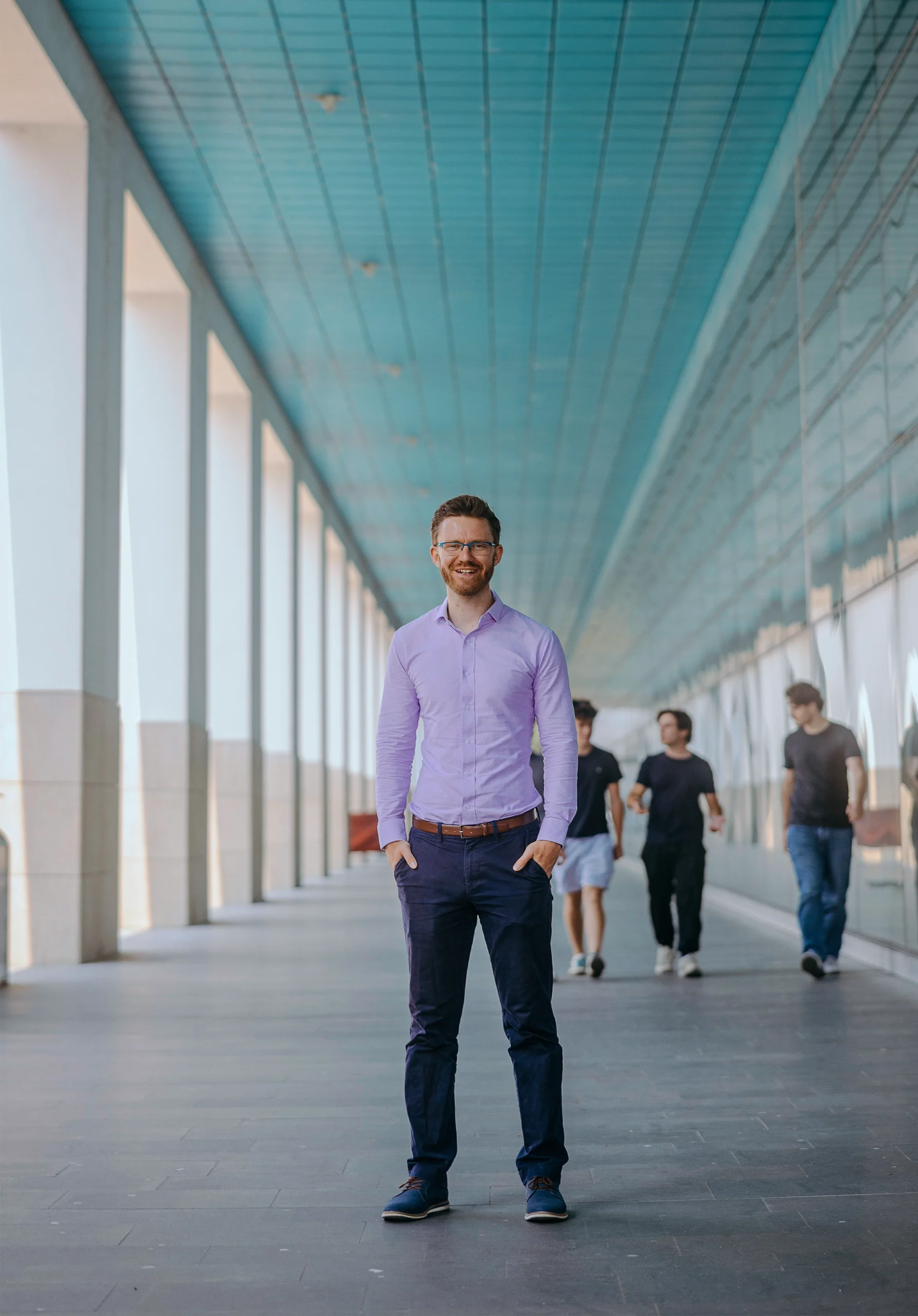Martin Schrimpf in a purple short and jeans stands in a long corridor