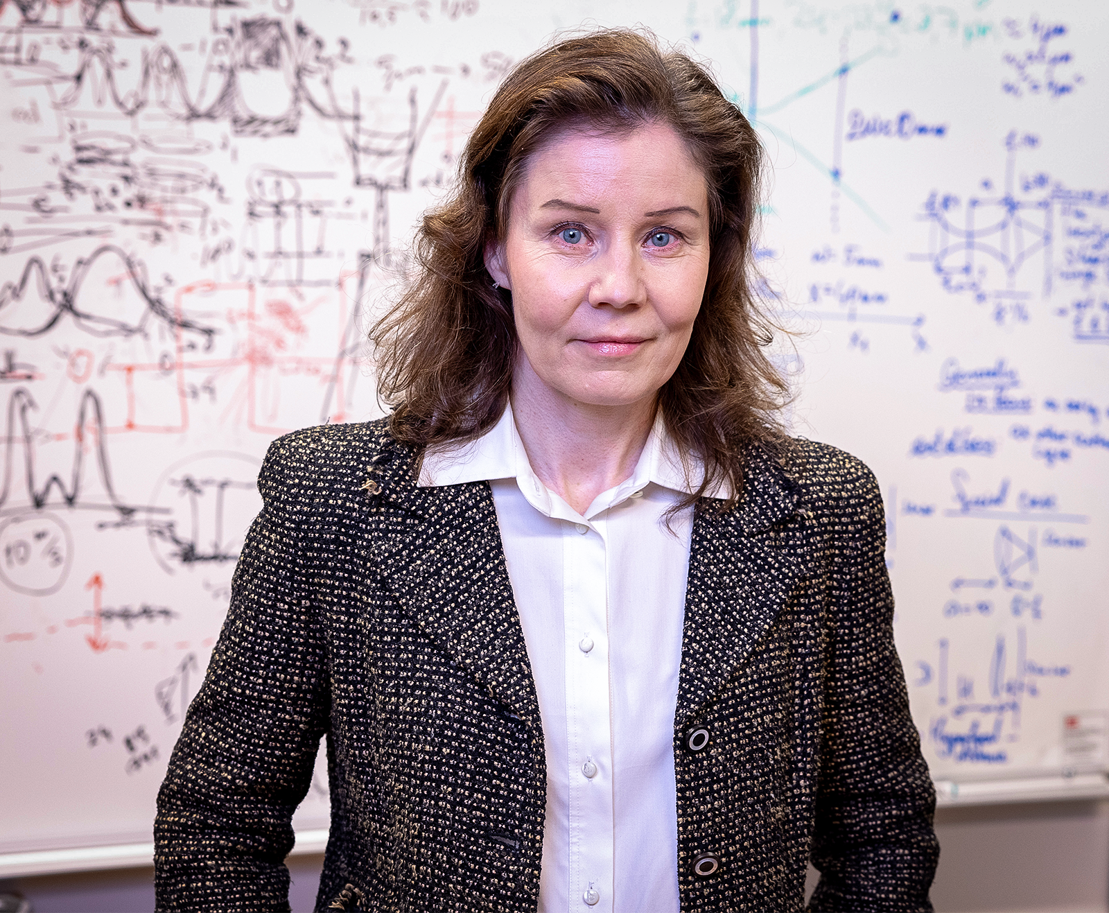 A woman in a tweed jacket stands in front of a whiteboard.