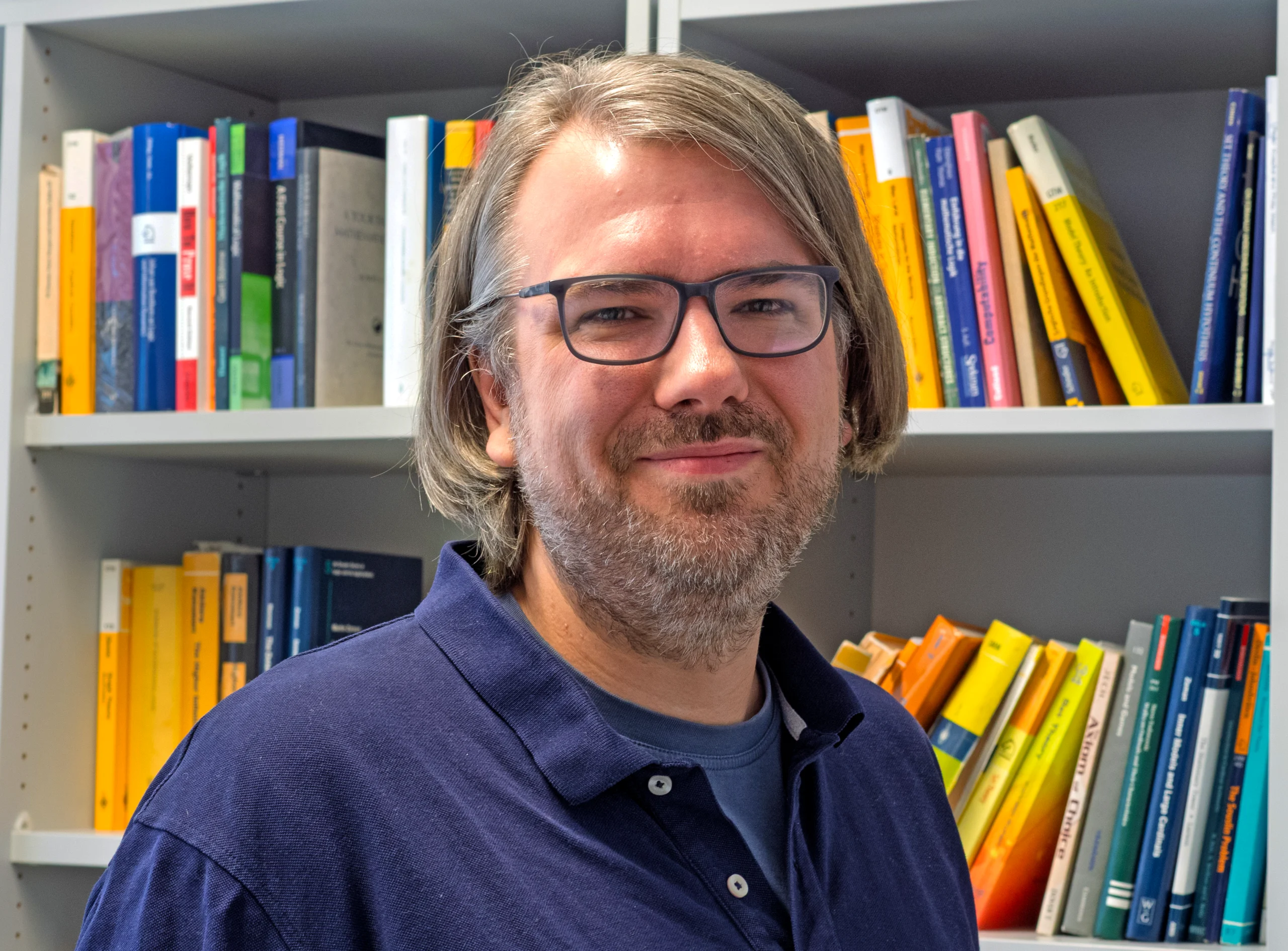 Man in glasses standing in front of a bookshelf.