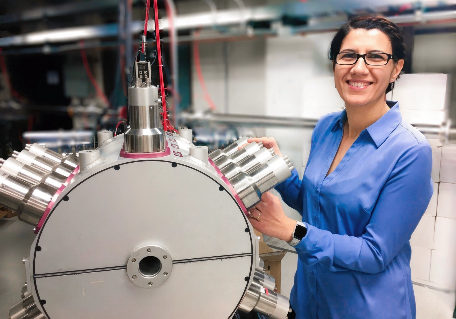 A woman poses with a shiny metal instrument with spokes emanating from it.