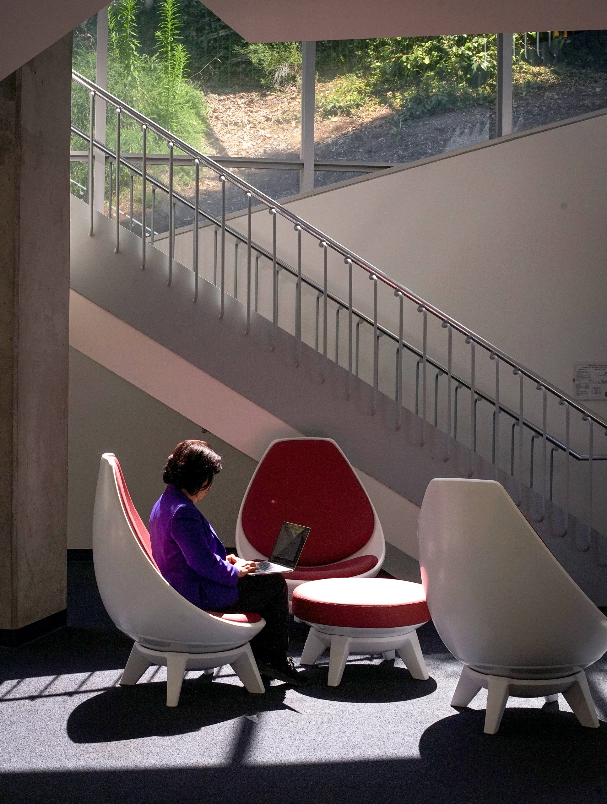Woman at a distance, sitting in a chair near a library staircase.