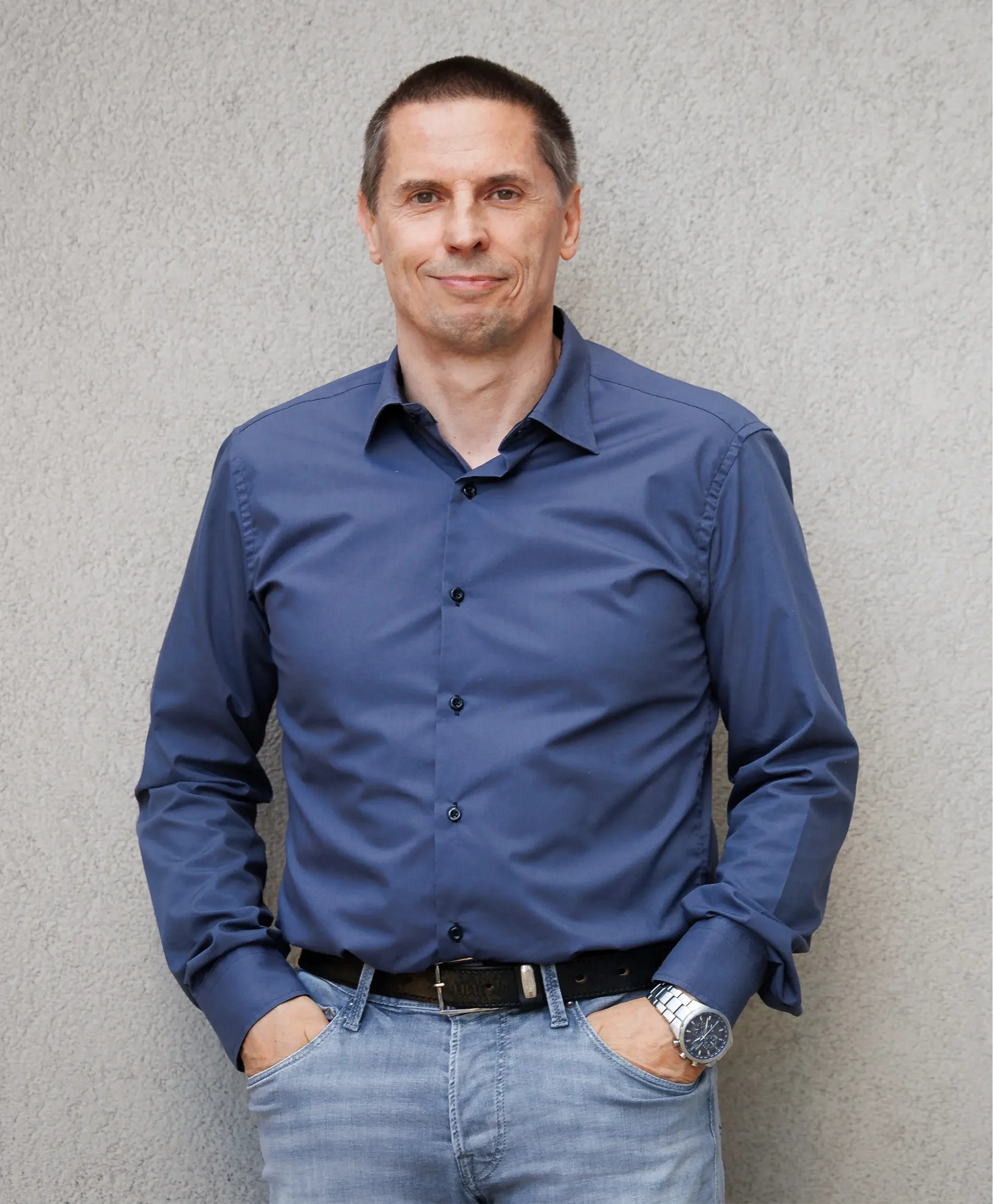 Man in a dark blue shirt standing in front of a gray wall.