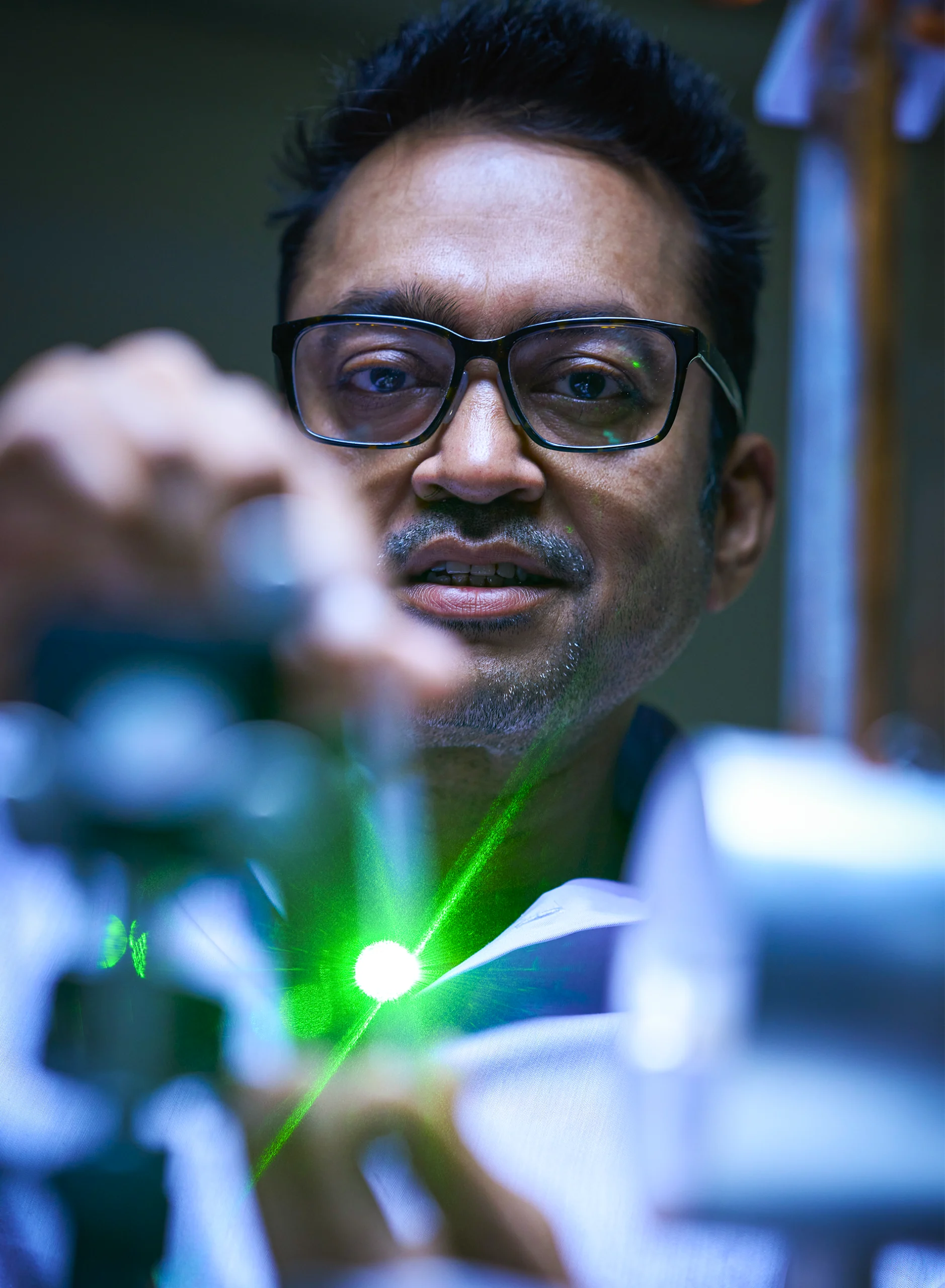 A man is seen working with a green laser in a dark laboratory.