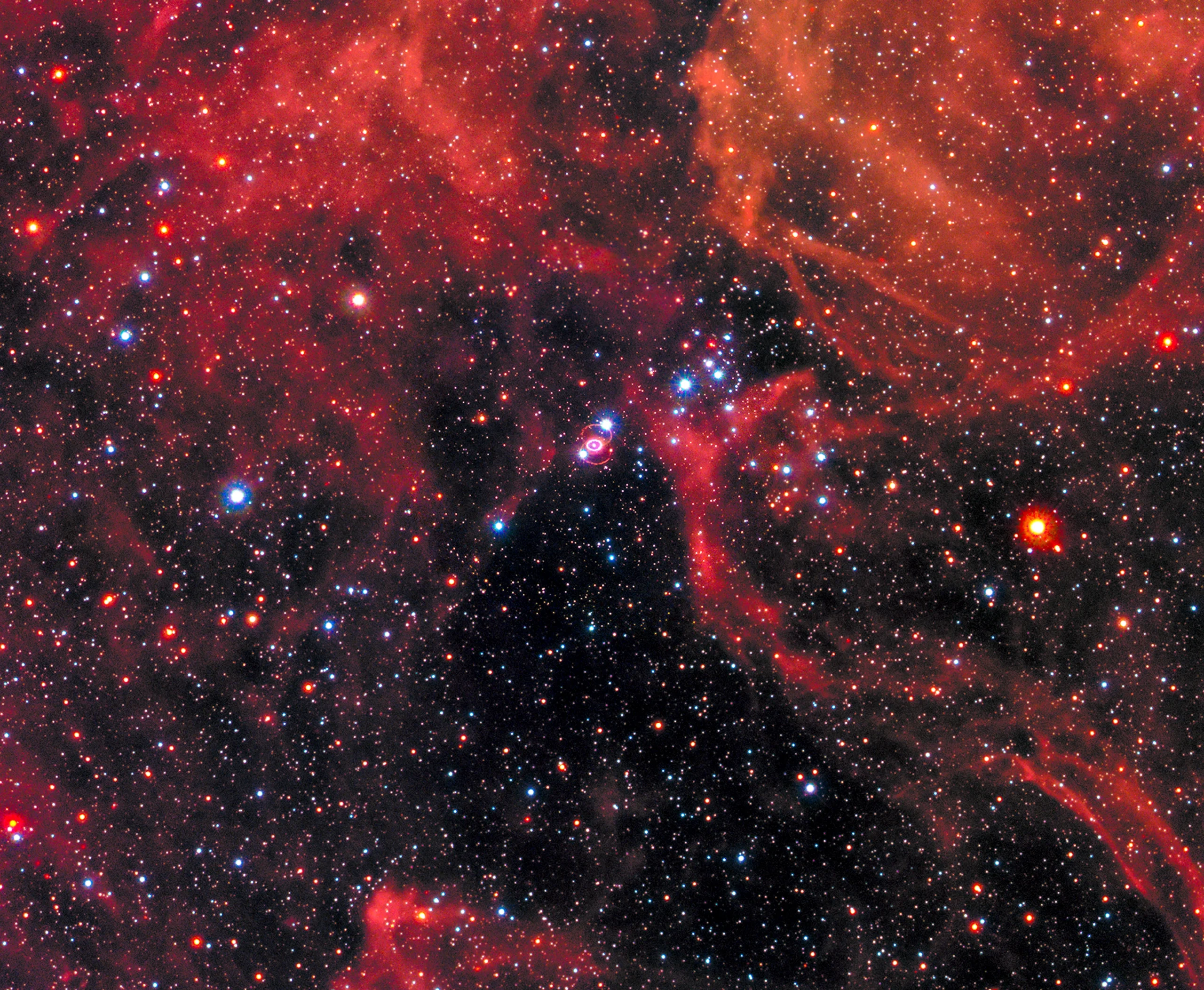 A photo of the night sky with a tiny ring-shaped supernova in the center.
