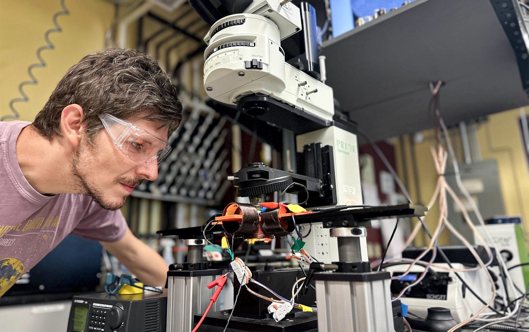 A man in protective glasses peers closely at some lab equipment.