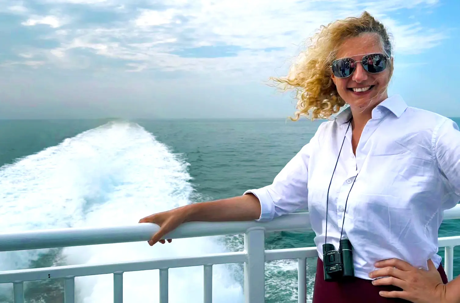 A woman wearing sunglasses stands on the deck of the Halunder Jet, her hair blowing in the wind.