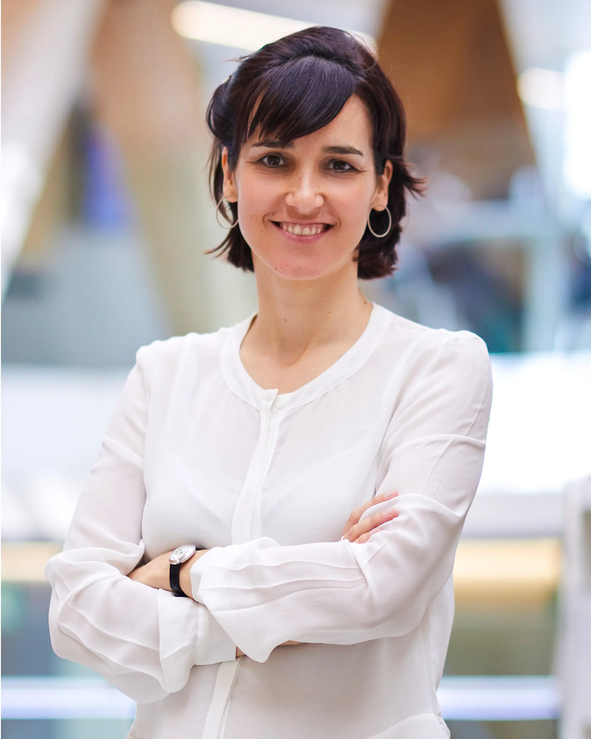 A woman wearing a white shirt stands with her arms folded.