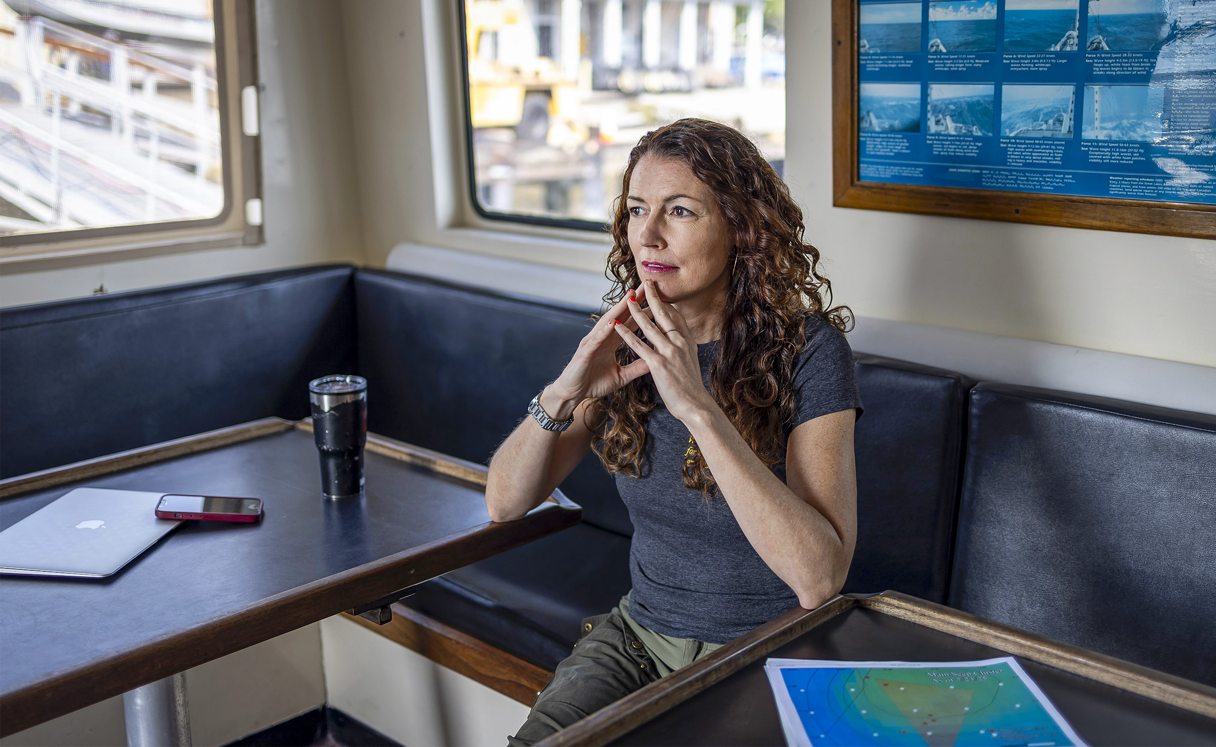 Lloyd sits inside a boat’s cabin, resting her chin on her folded hands and staring into the middle distance.