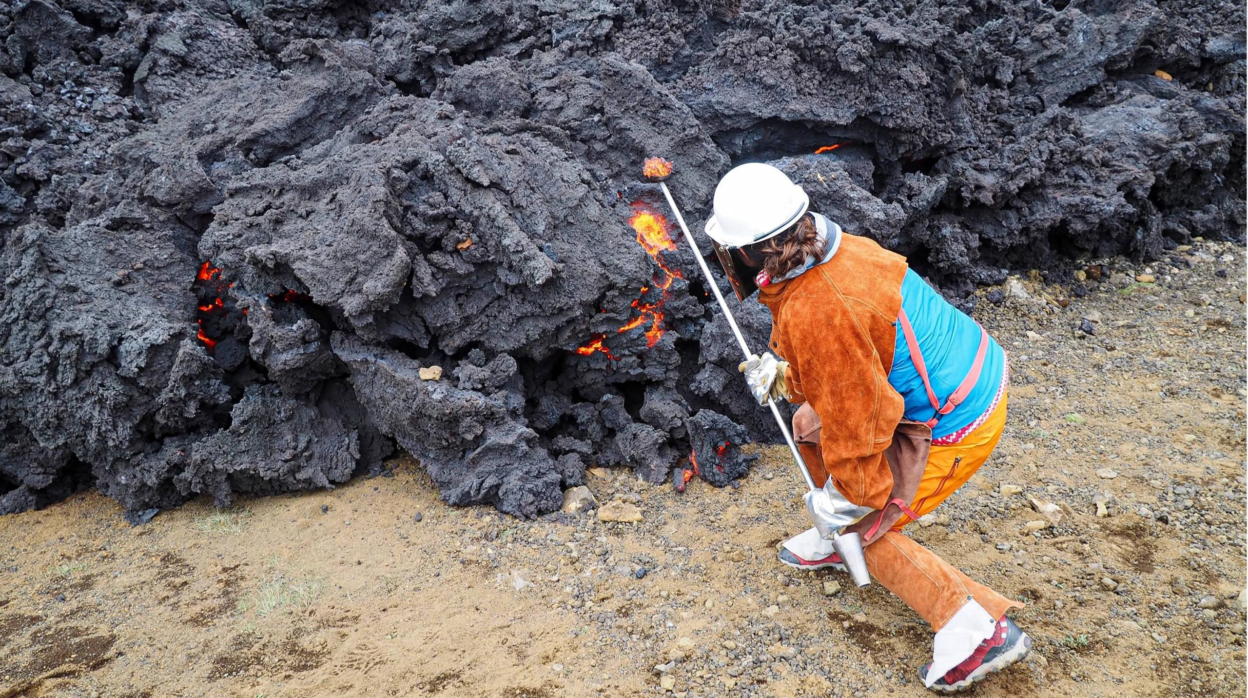 Lloyd, wearing safety equipment, uses a long pole to scoop some hot lava off an advancing floe.