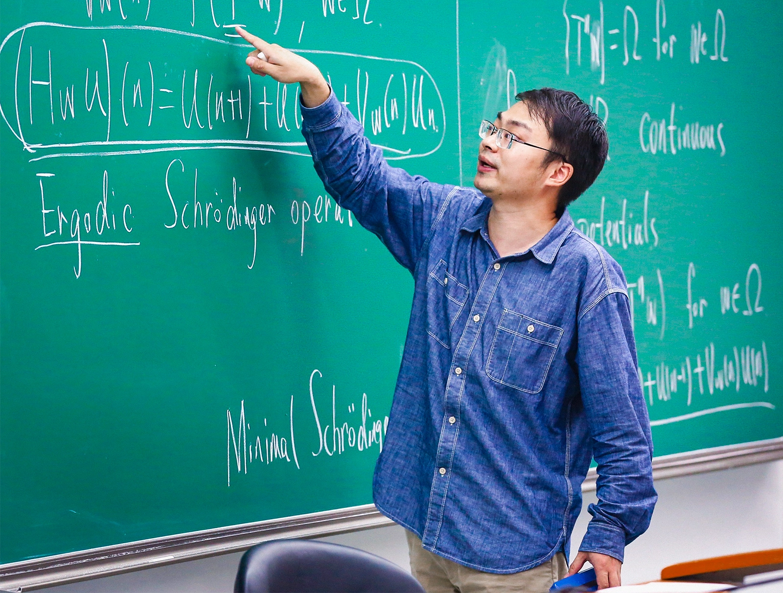 Man in a dark blue shirt standing in front of a bookcase.