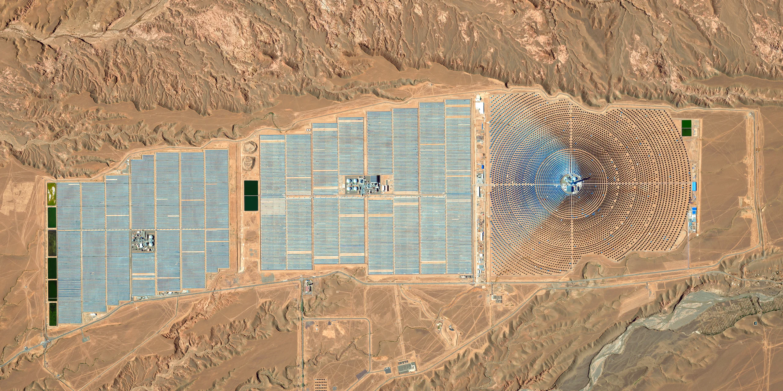 Вид сверху на огромную солнечную электростанцию, включающую множество концентрических колец и рядов солнечных панелей.