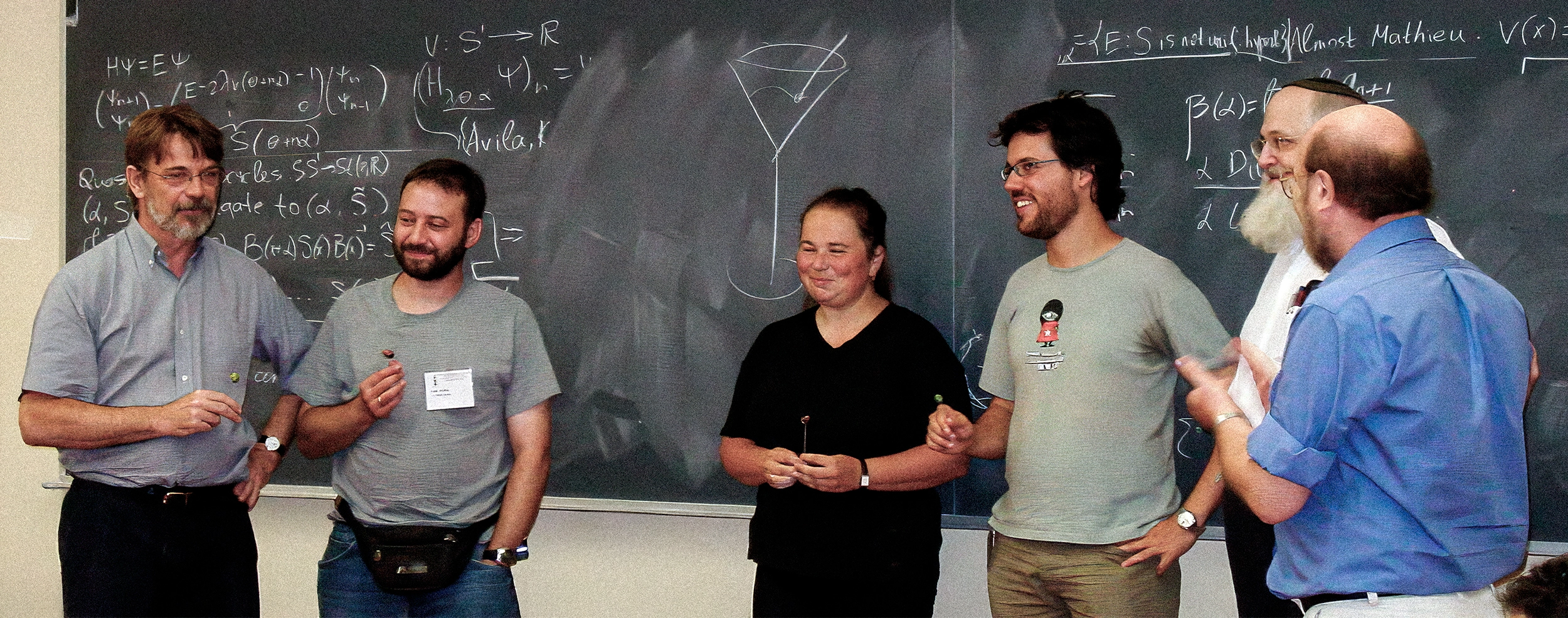 A group of mathematicians standing in a classroom holding martini stirrers.