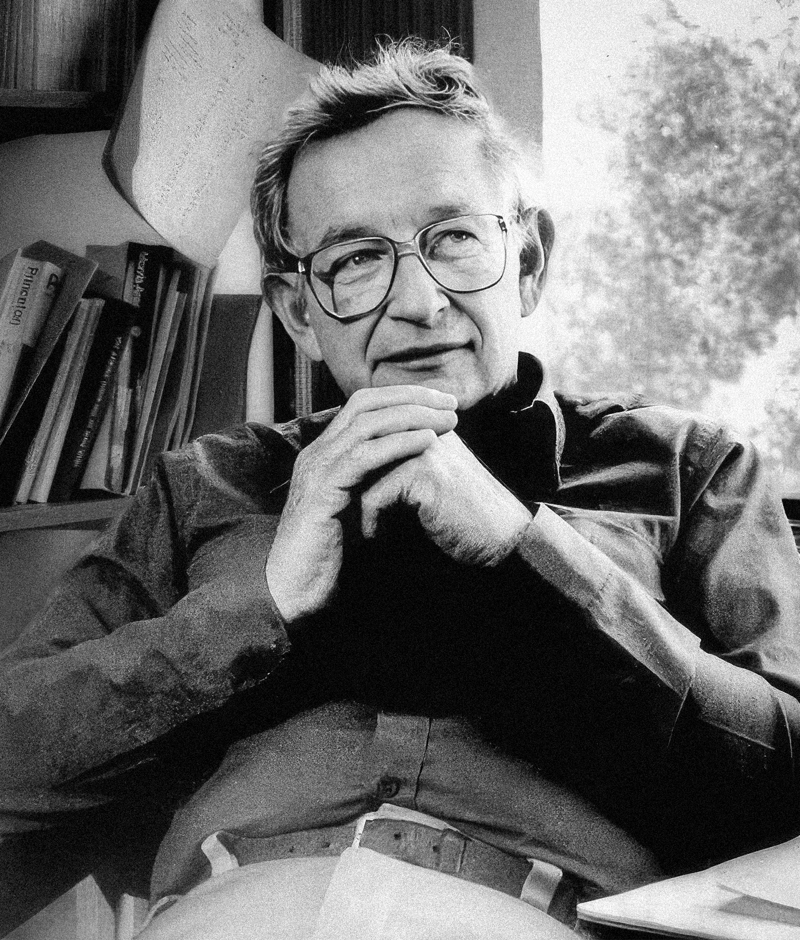 Black-and-white photo of a man in glasses, holding his hands in front of him.