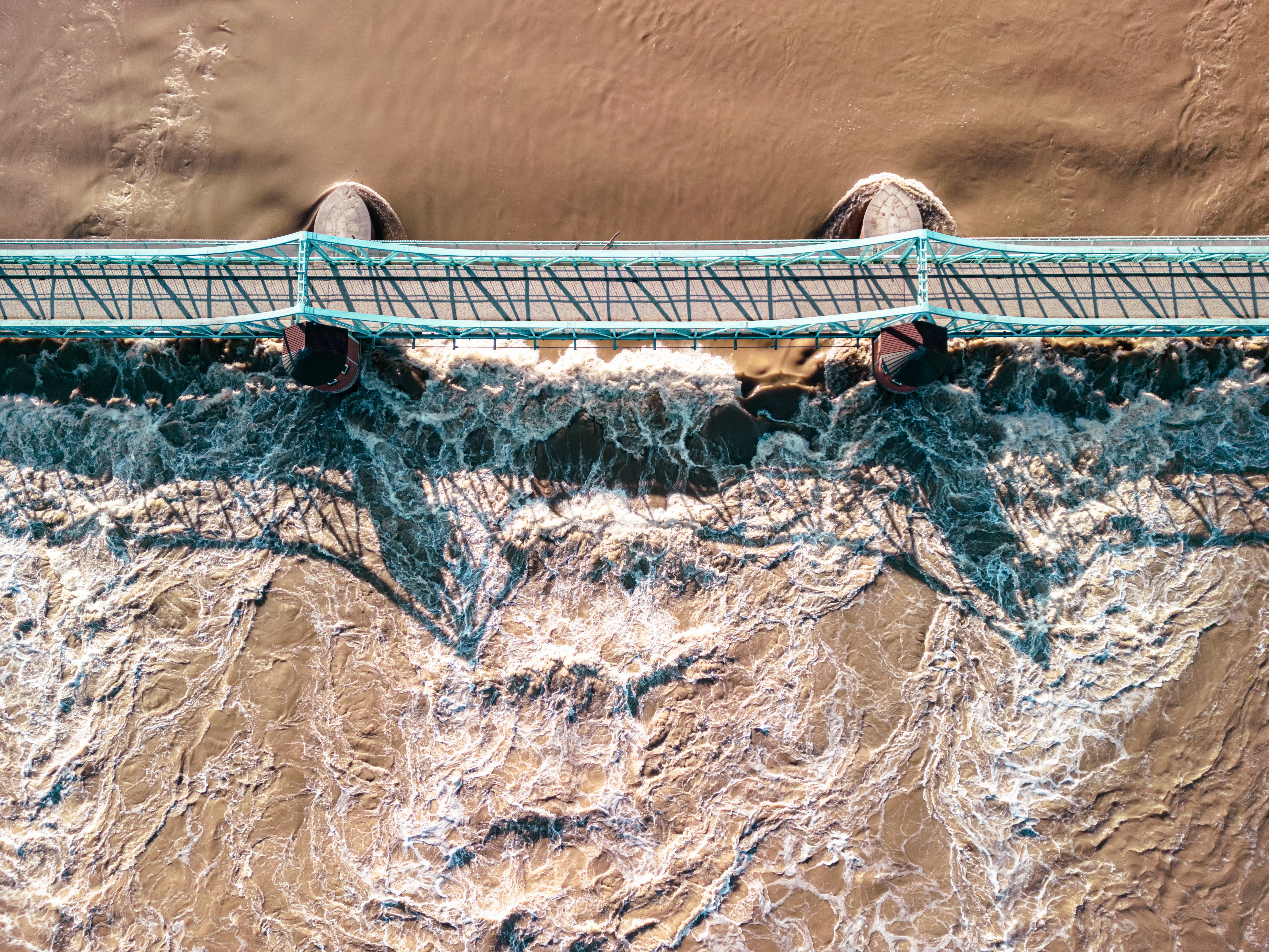 Aerial photo of brown floodwaters flowing under a truss bridge.