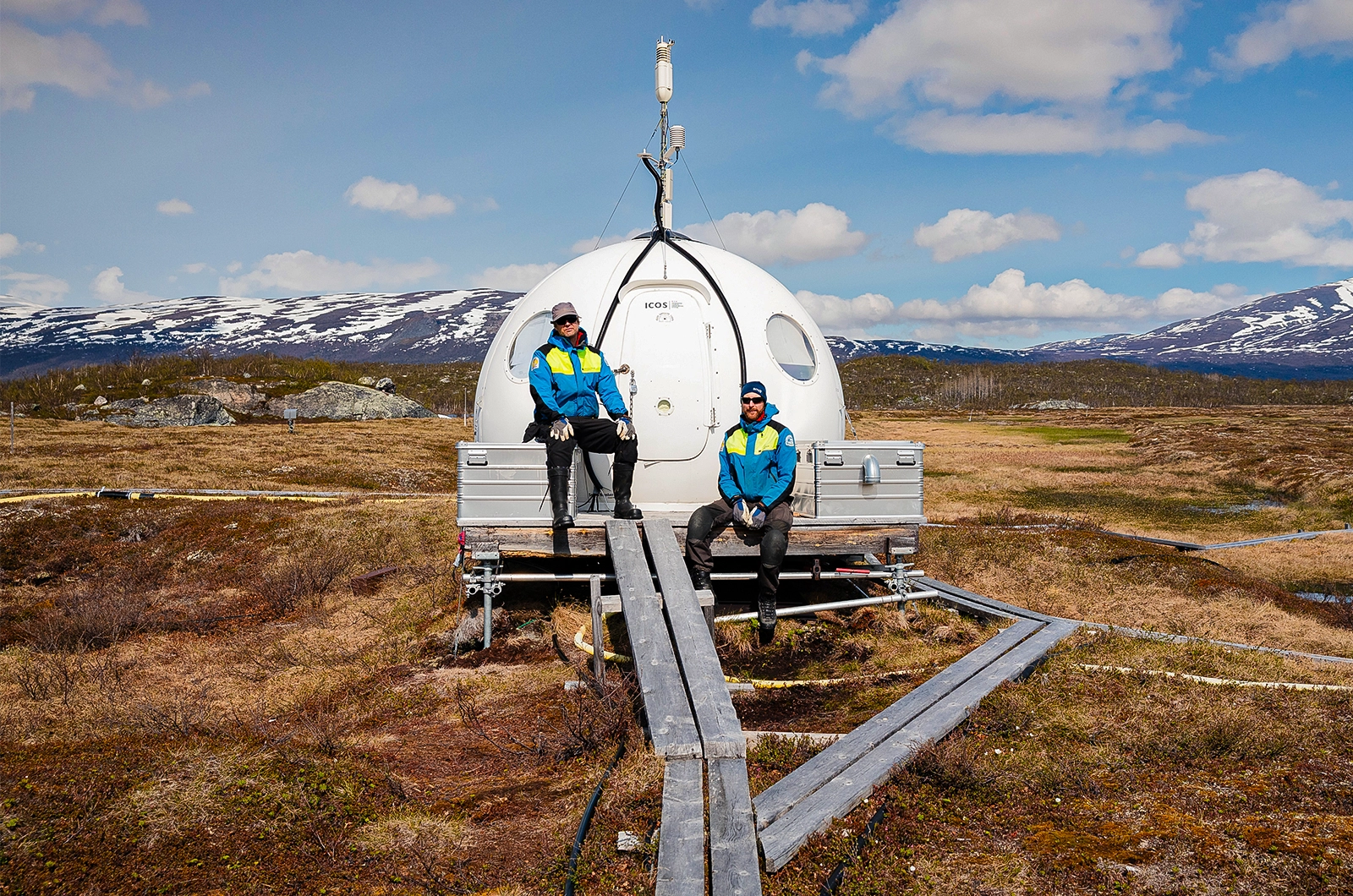 Two researchers rest on the station with mountains in the background.