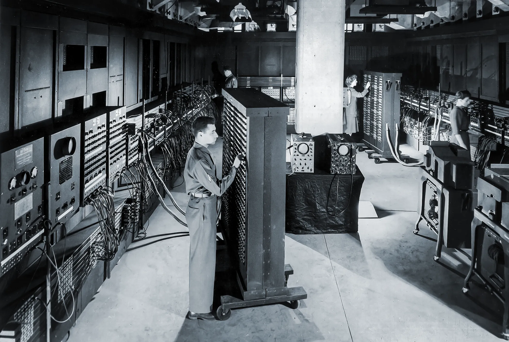 A black-and-white photo of an army corporal setting switches on a room-size computer.