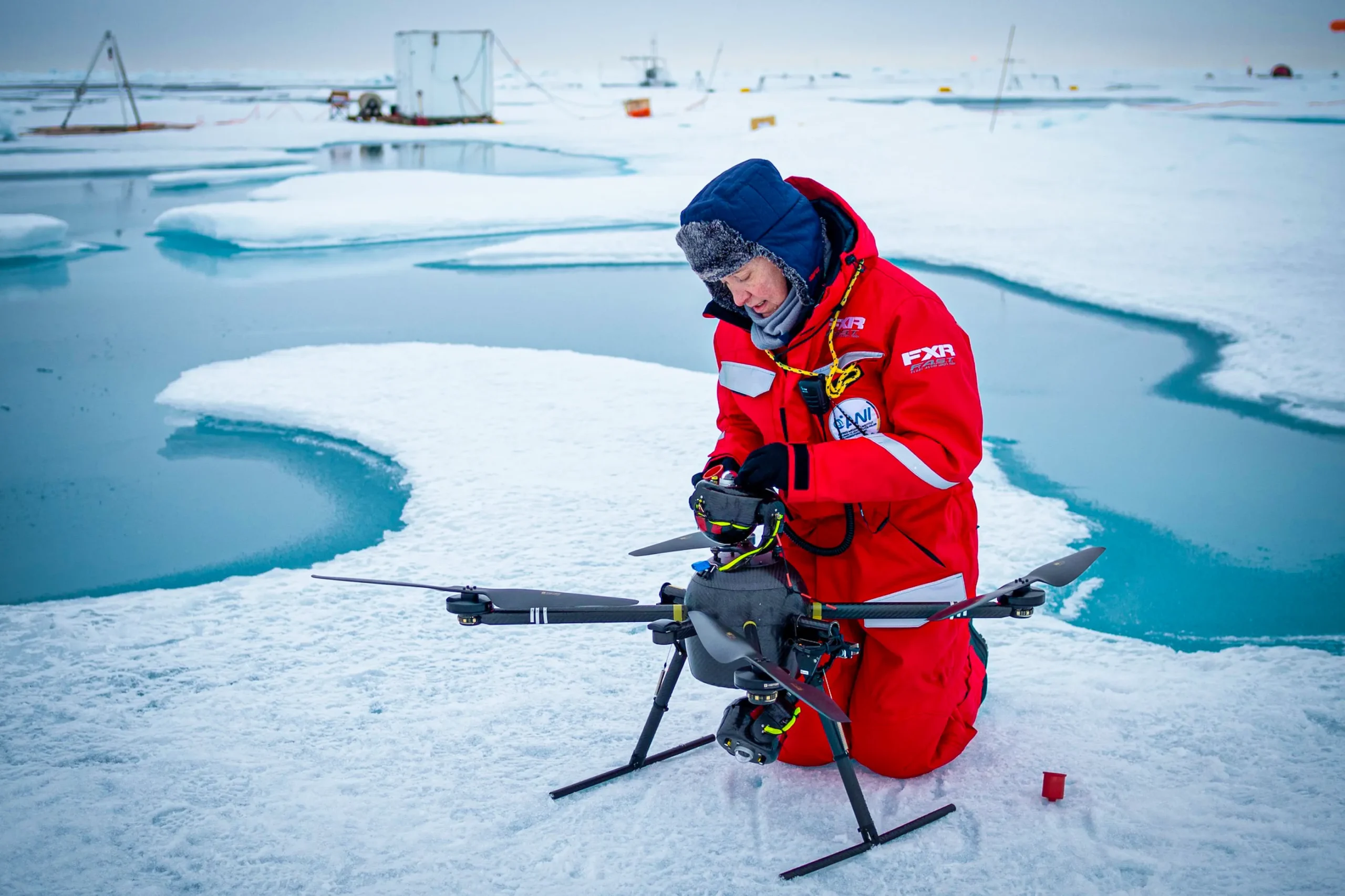 A researcher kneels next to a drone on the ice.