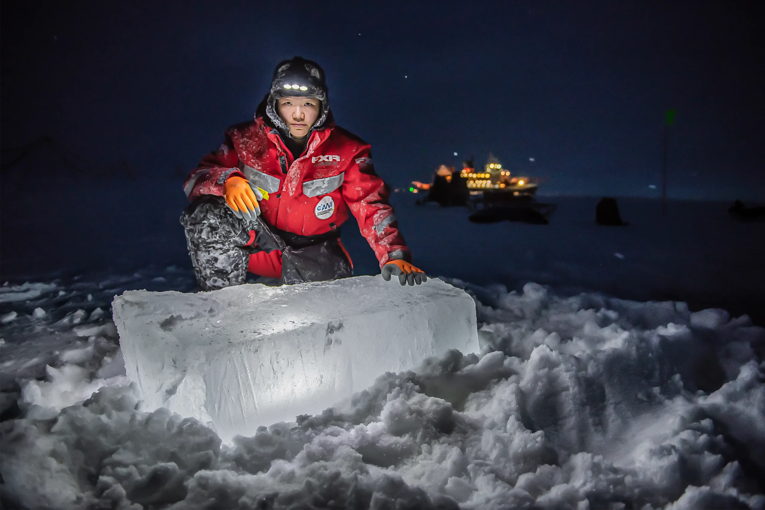 A researcher kneels next to a large block of ice in the dark.