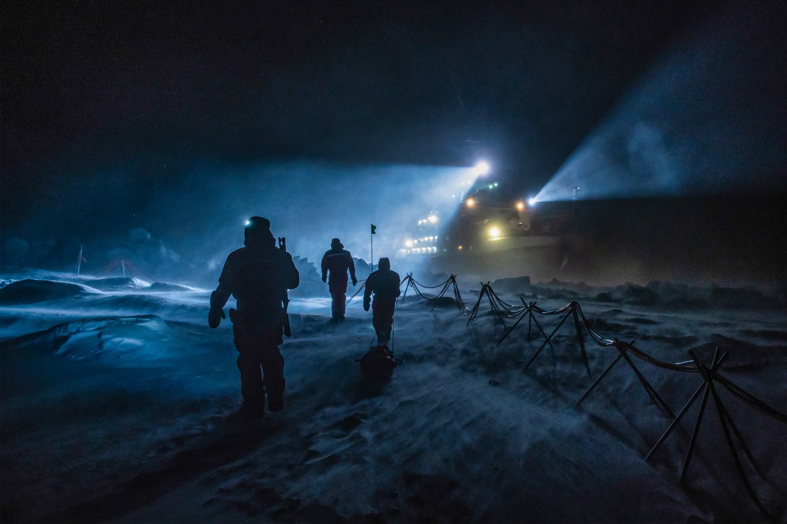 Three researchers walk toward the ship in a storm in the dark.