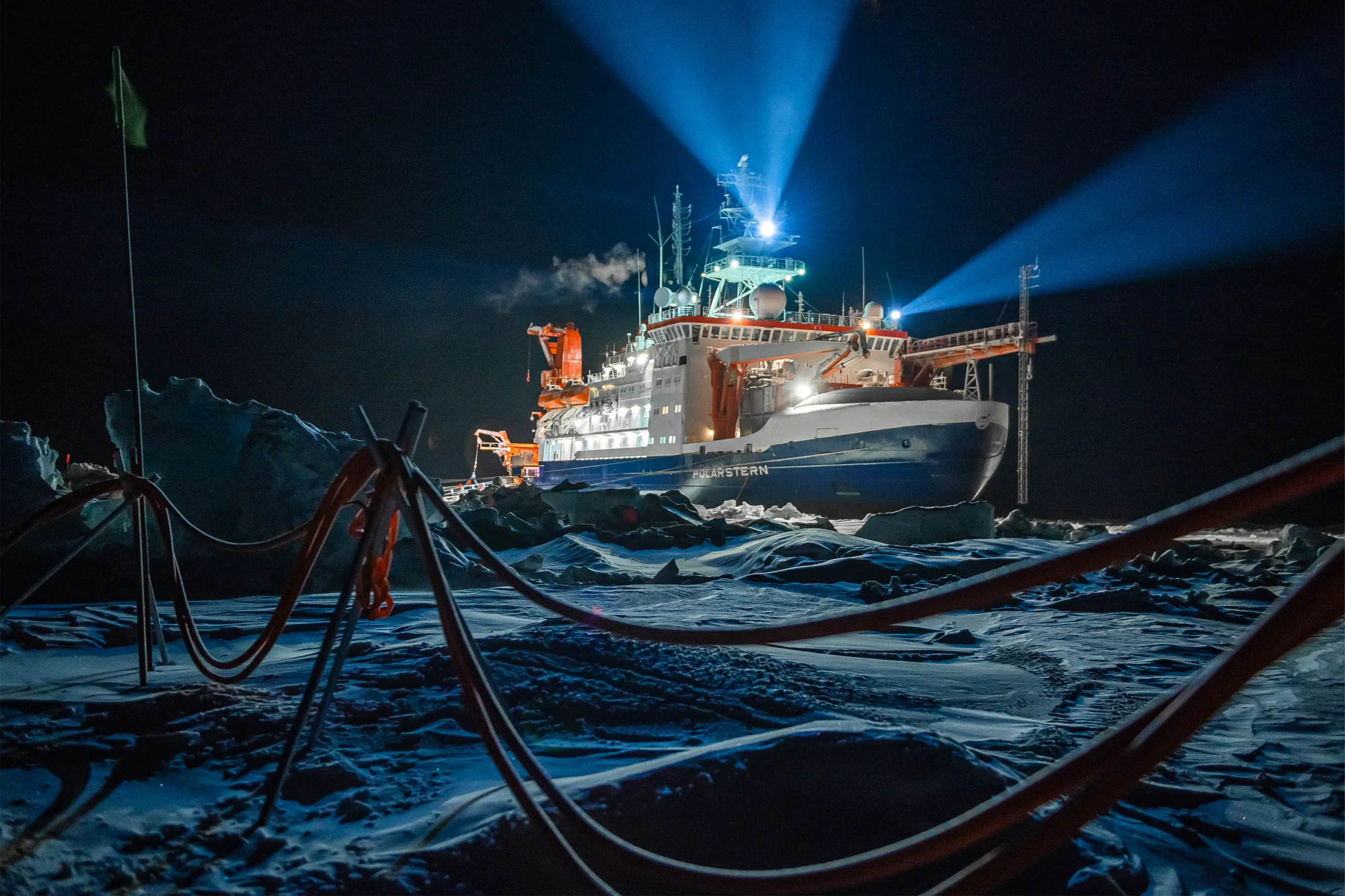 A ship sits in the ice in the dark.