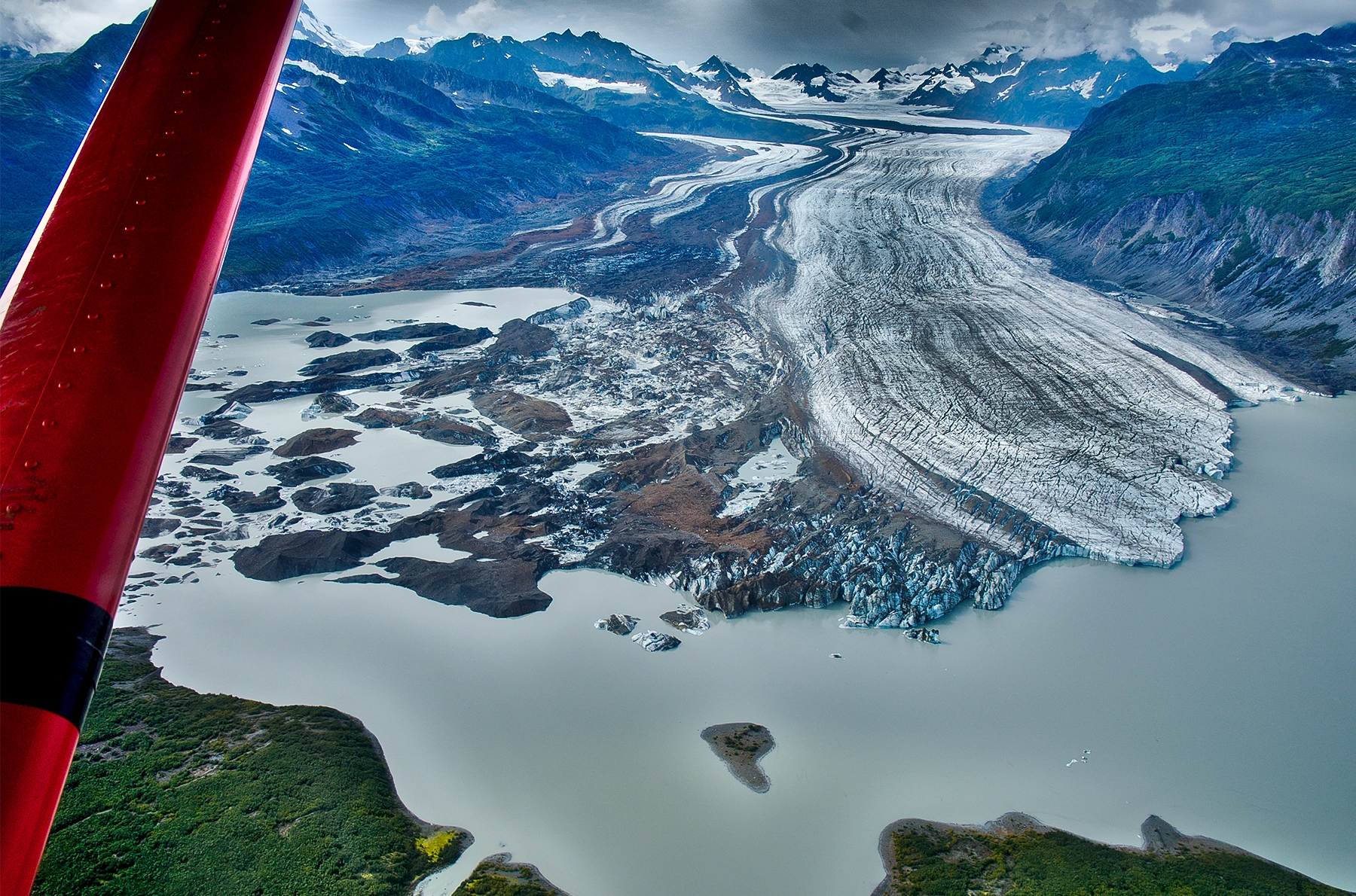 The red wing of an airplane juts over a lake and glacier.