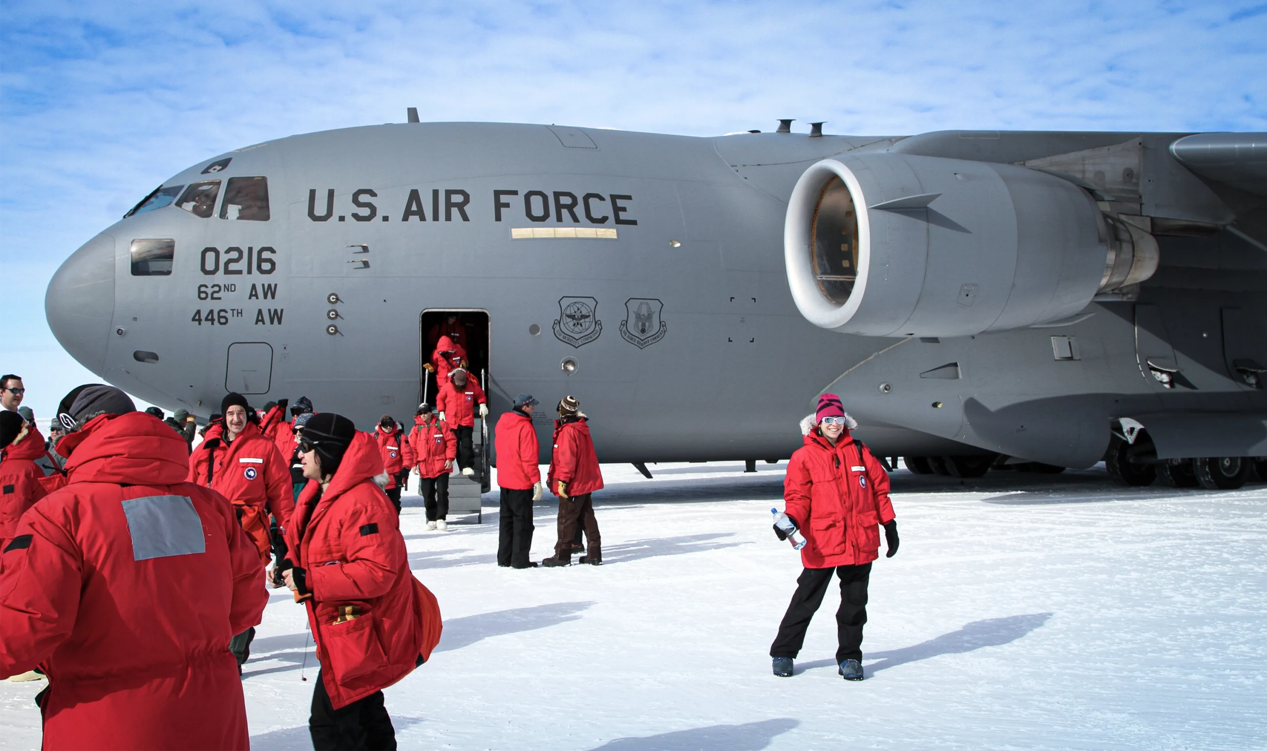 Scientists in red winter coats stand in front of a U.S. Air Force plane.