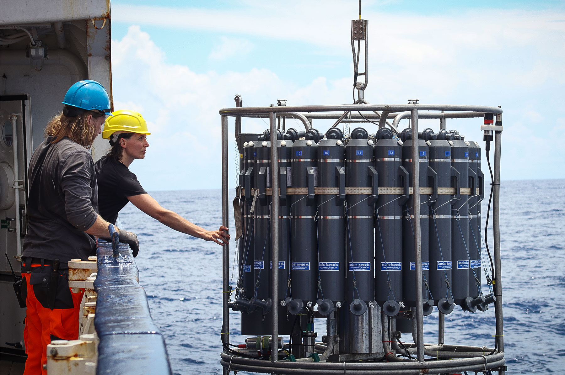 Two researchers lower a cylindrical instrument into the water.