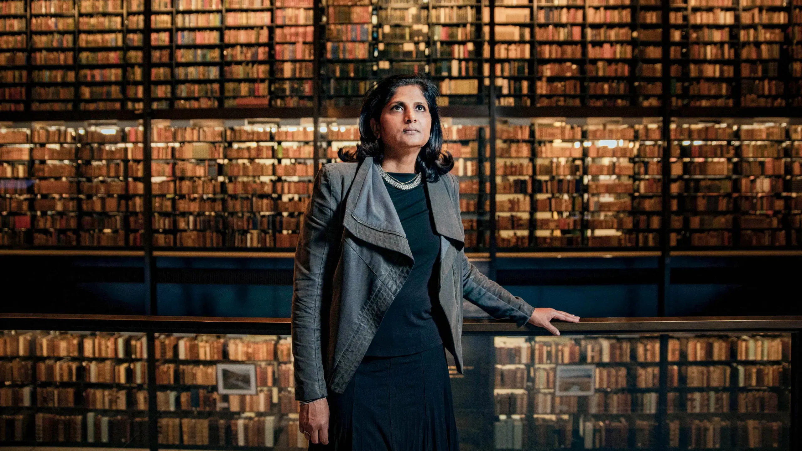 A woman stands in a library in front of a wall of books.