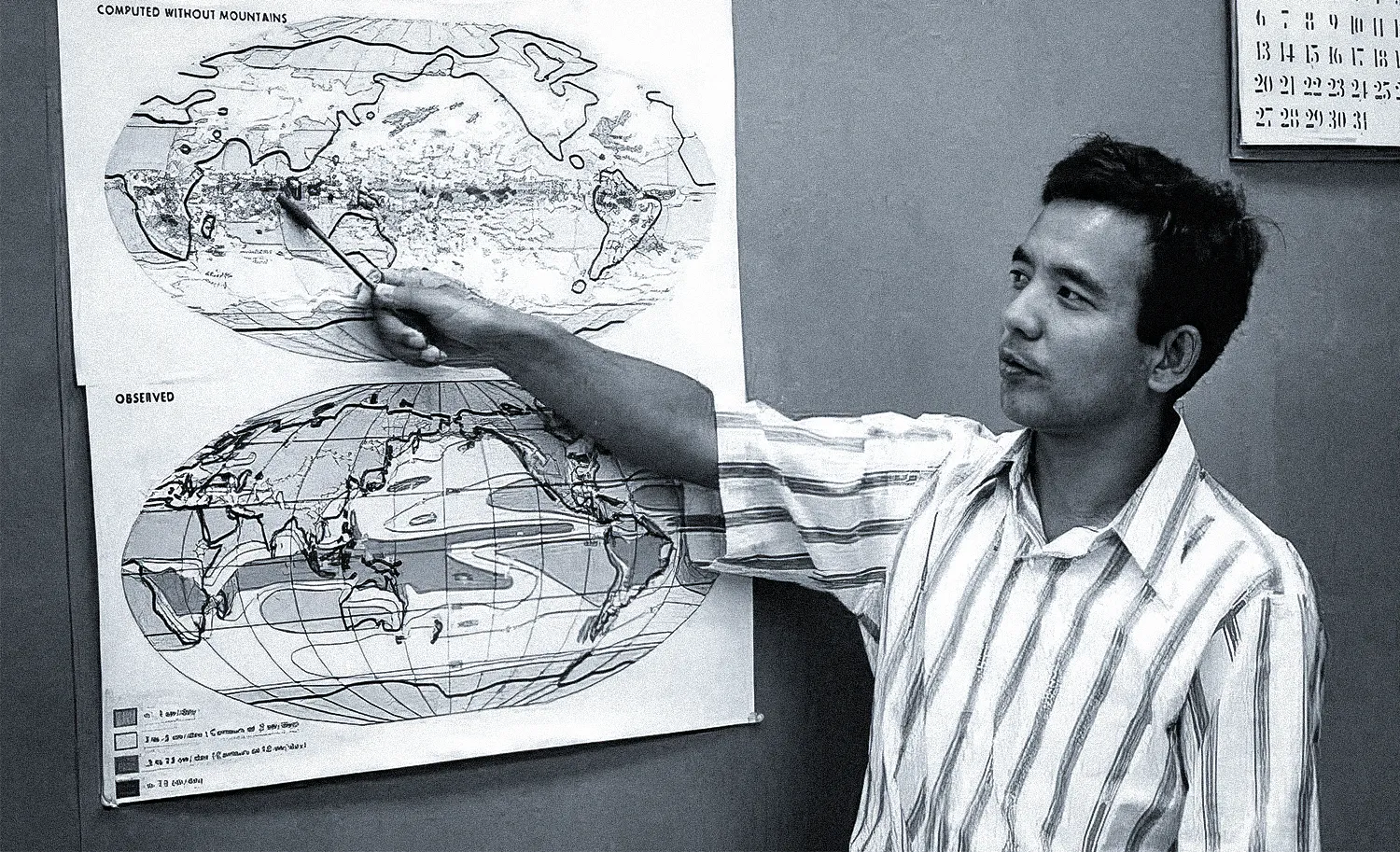 A picture of a young man in a striped shirt pointing a pencil at a map of Earth.