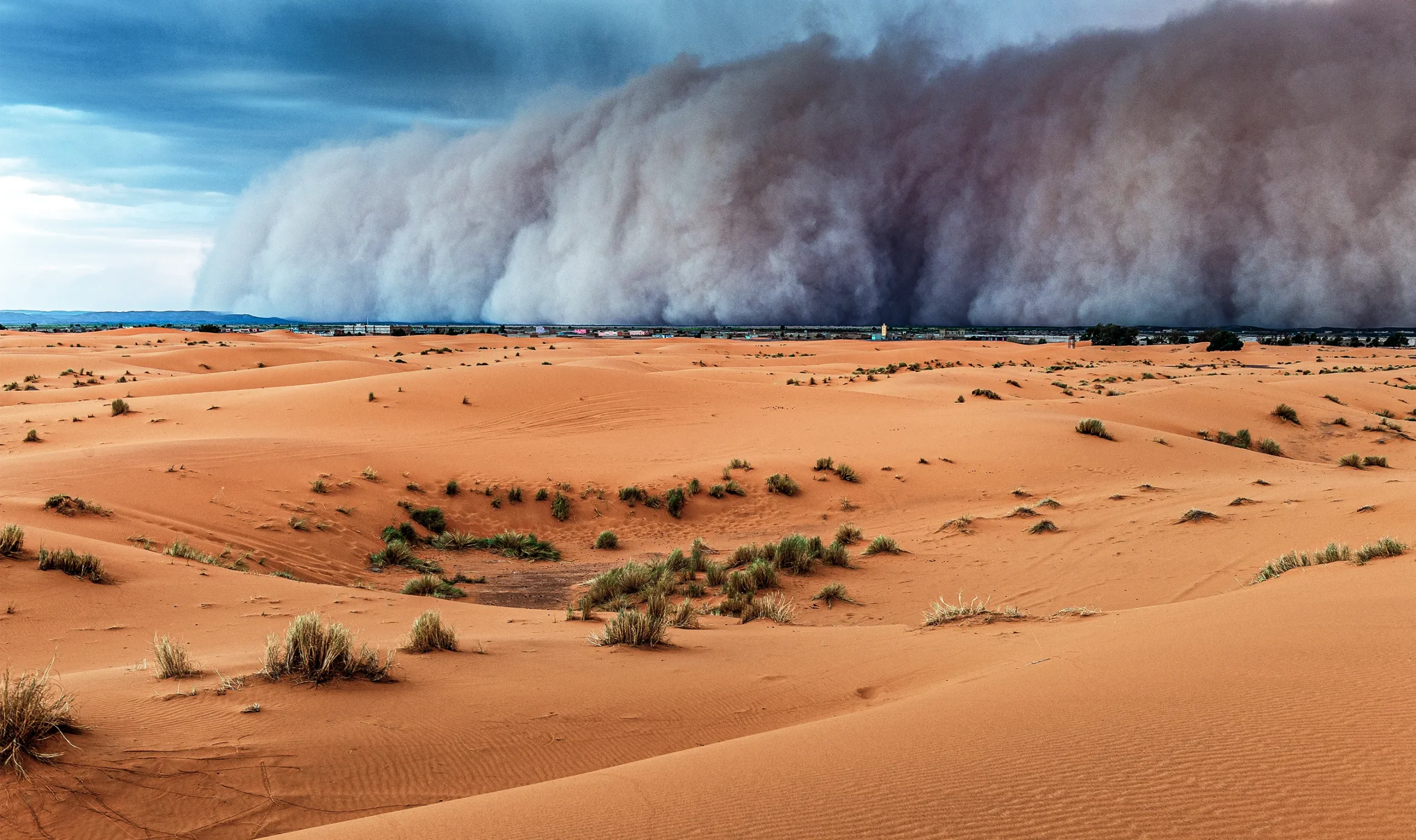 A wall of dust sweeps across a desert landscape.