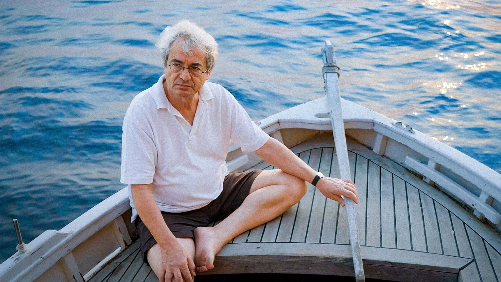 A man steering a small wooden sailboat.