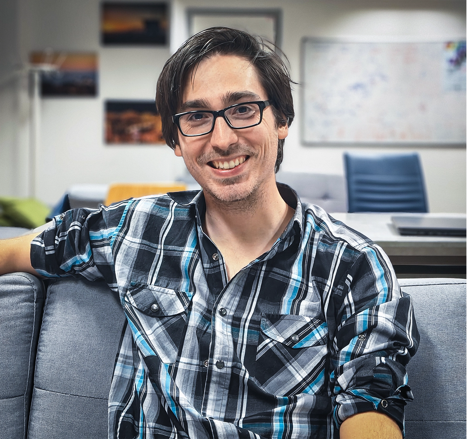 A smiling man with glasses sitting on a couch
