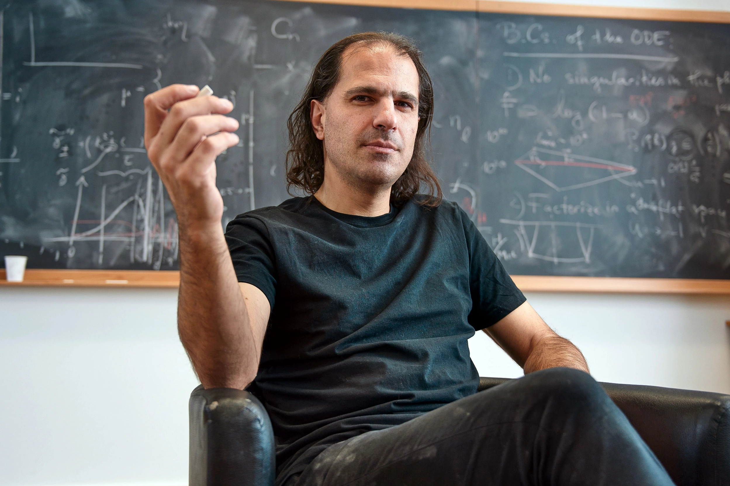 A man with shoulder-length hair sitting in a chair.