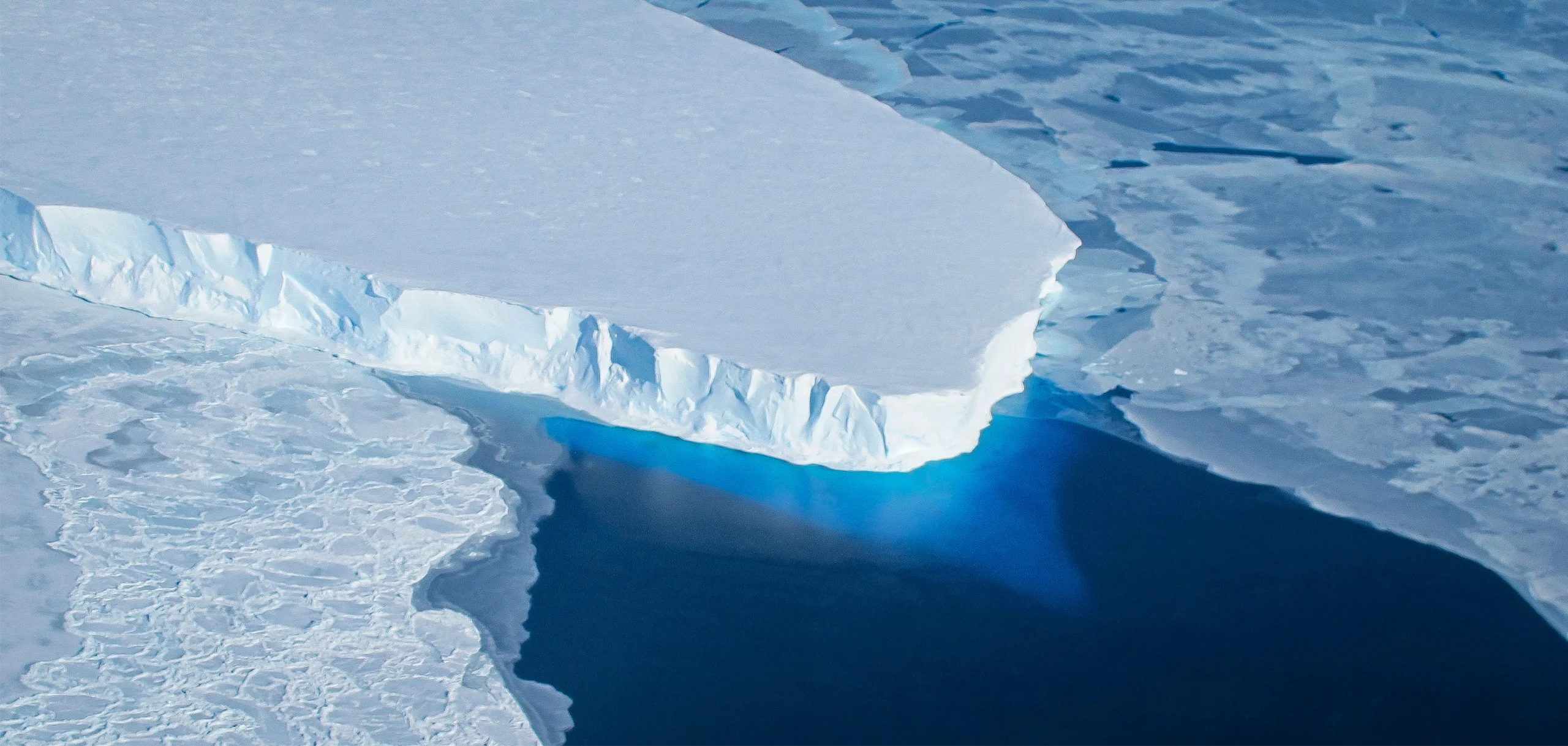 A satellite image showing the cliff edge of an ice shelf that floats in the dark ocean.