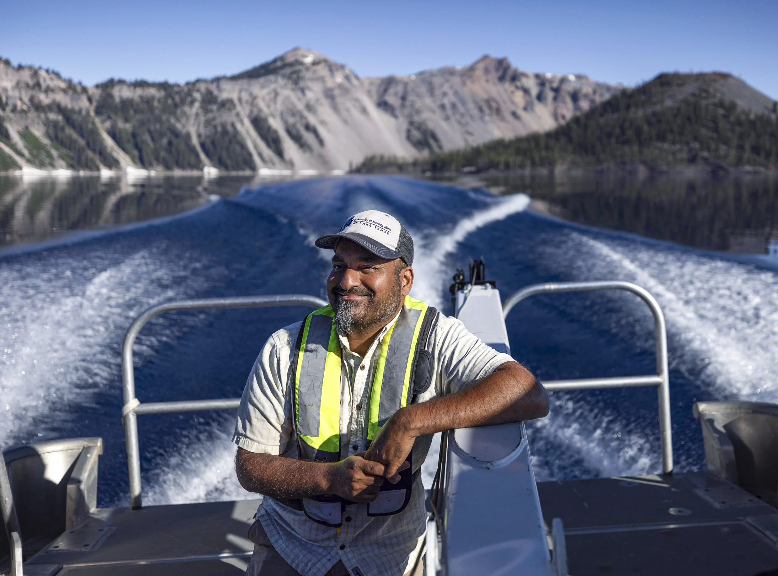 Sudeep Chandra stands at the back of a research vessel motoring across Crater Lake.