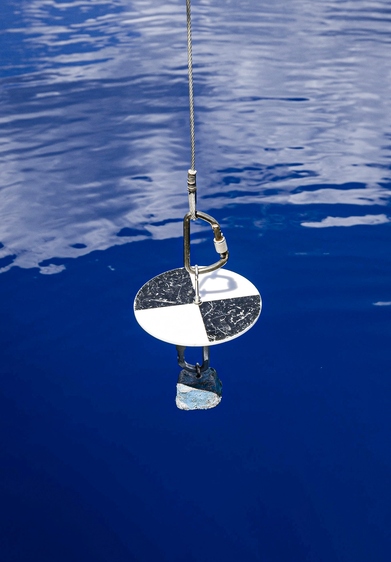 A circular black-and-white disc is suspended by rope over the water.