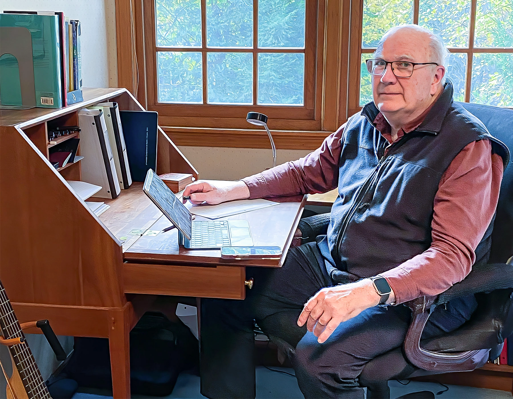 A man sits at a wooden desk in front of a window.