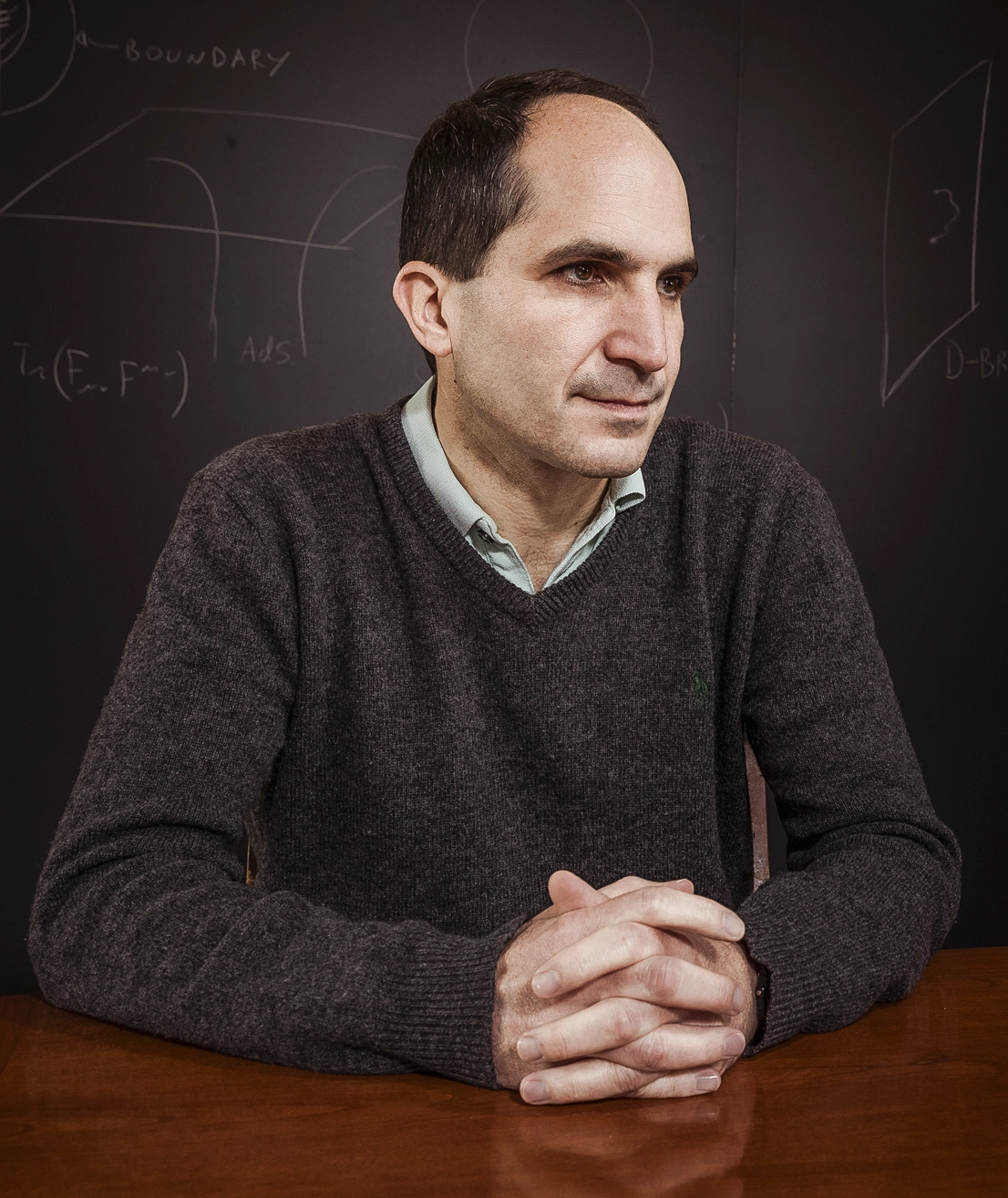 A man in a brown sweater at a desk.
